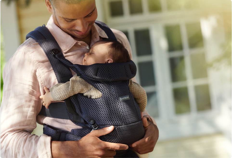 Dad wears and holds newborn in a Baby Bjorn baby carrier.